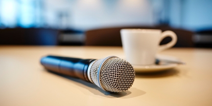 Stemning på pressekonferanse: mikrofon og kaffekopp på et bord.